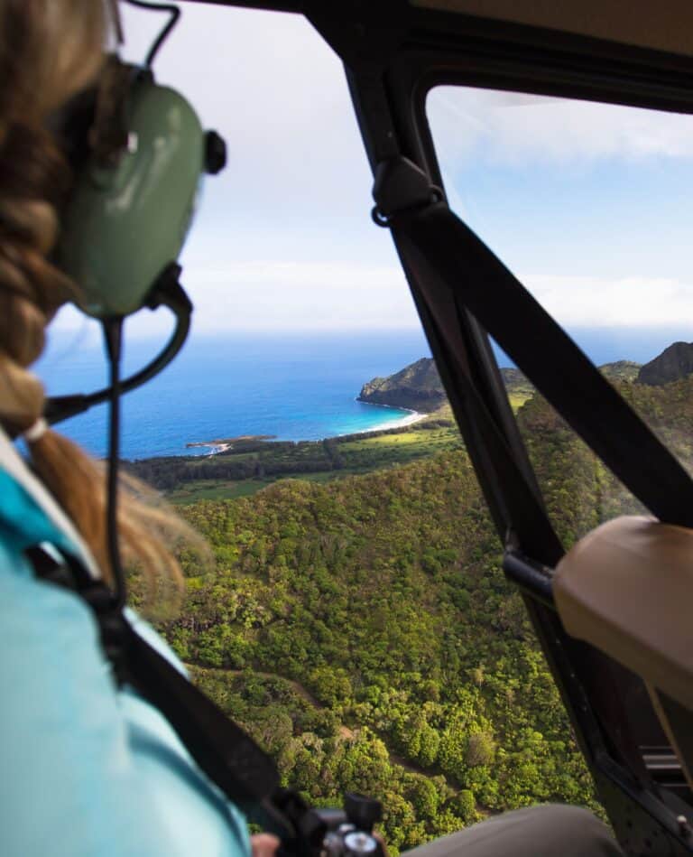 A woman gazes out the window of a helicopter, with the Hawaii visible below.