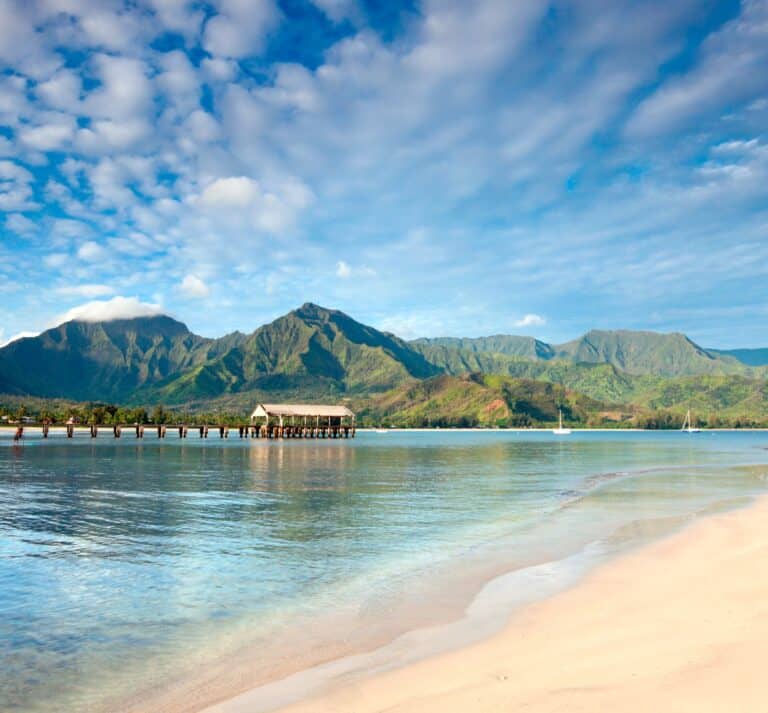 A beautiful Hawaiian beach framed by towering mountains in the distance, showcasing a serene coastal landscape.