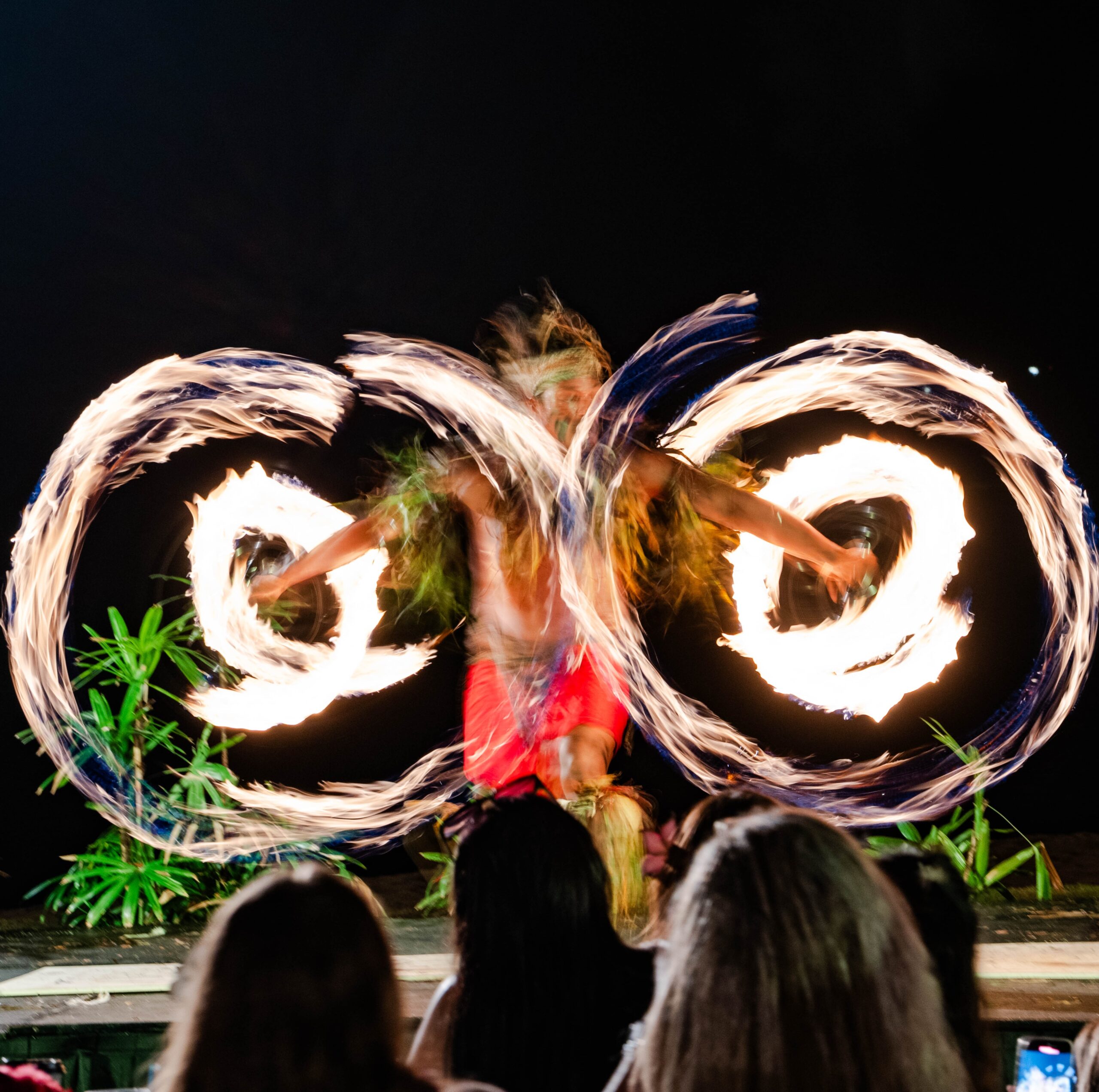 A performer spins glowing fire rings at night, creating a mesmerizing display of light and movement against the dark sky.