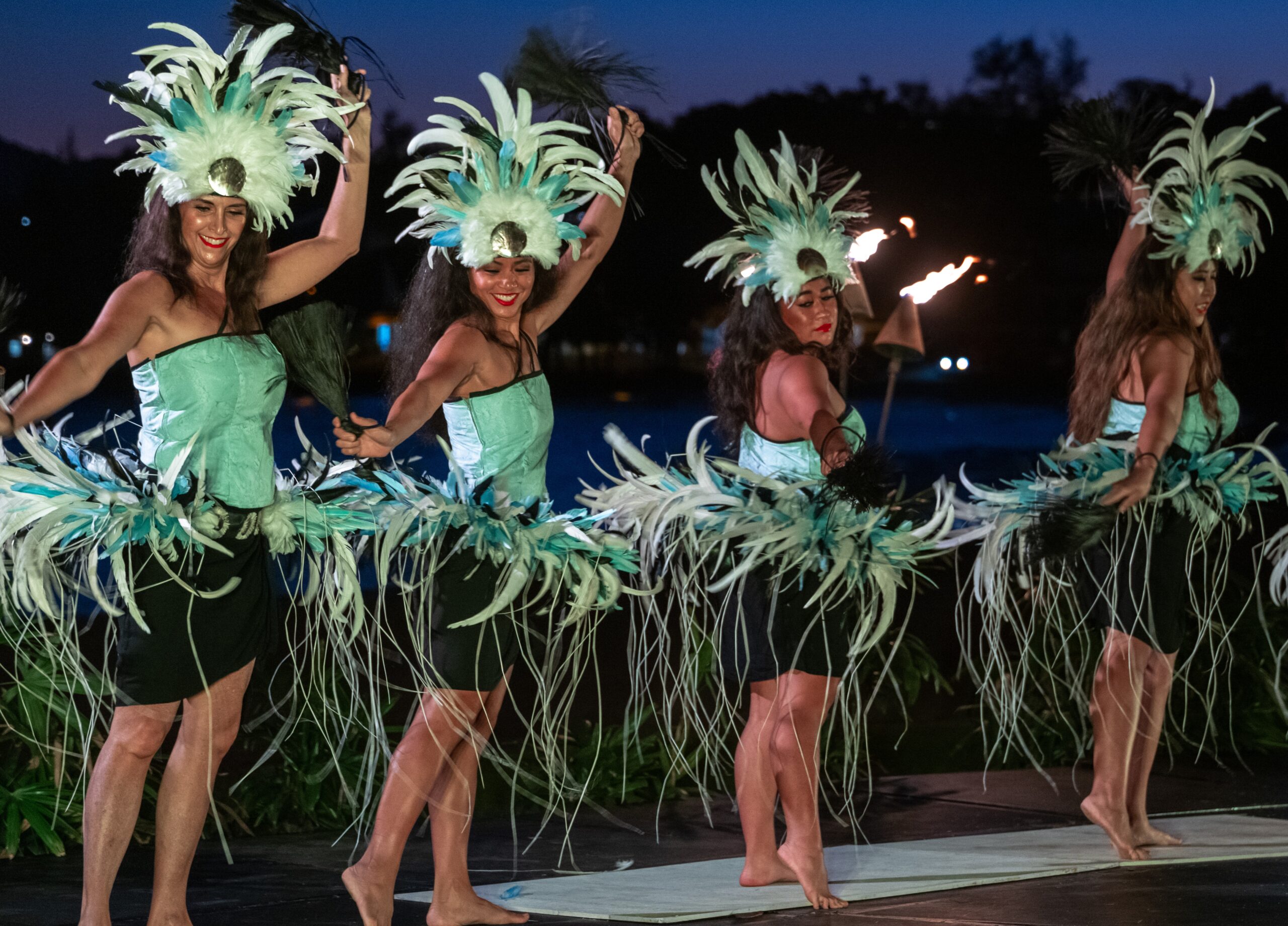 A night scene featuring dancers in green costumes, gracefully performing with a backdrop of darkness and subtle lighting.